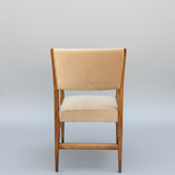 Back side of Beige cushioned chair with wooden frame against a gray wall.