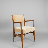 Wooden armchair with beige cushion against a gray wall from an angle.