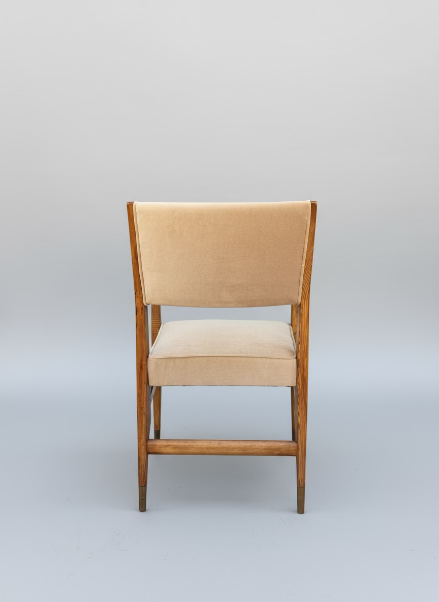 Back side of Beige cushioned chair with wooden frame against a gray wall.